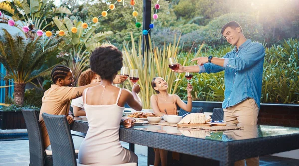 Cheers, celebrate, and friends at dinner in garden at party and diversity, food and wine at outdoor event. Glass toast, men and women at table, fun people with sunset drinks in backyard together