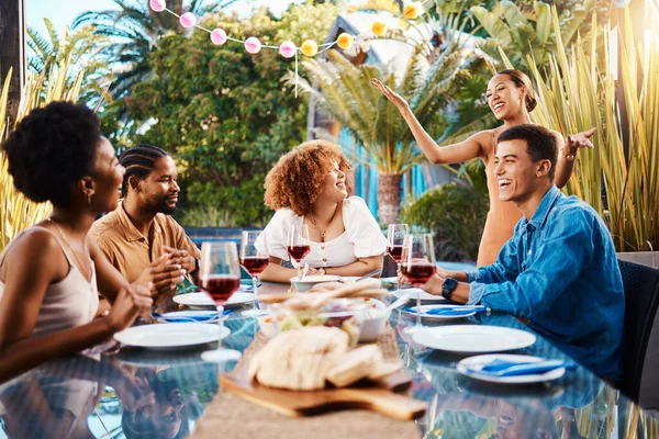 Friends, food and eating outdoor at a table for social gathering, happiness and holiday celebration. Diversity, men and women group at lunch, party or reunion with drinks in garden for fun and relax.