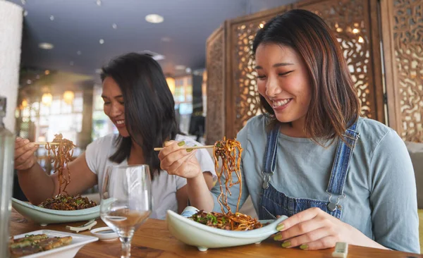 Restaurant, girl friends and smile with food, noodles and cafe happy from bonding. Asian women, eating and plate together with friendship at a table hungry with chopsticks at Japanese bar gathering.