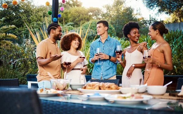 Talk, friends at dinner in garden at party and celebration with diversity, food and wine at outdoor event. Conversation, men and women at table for lunch, fun people with drinks in backyard together