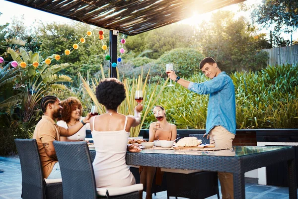 Cheers, group of friends at dinner in garden at party and celebration with diversity, food and wine at outdoor party. Glass toast, men and women at table, fun people with drinks in backyard together