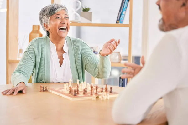 Laughing, game and senior couple with chess in a house in retirement for a competition. Happy, together and a funny and elderly man and woman with a board for a challenge or bonding with conversation.