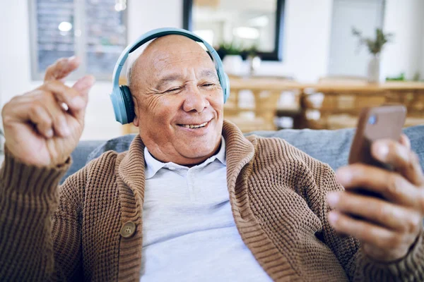 Phone, senior man and watch music video, streaming podcast and reading happy story, news article or retirement blog. Home, smartphone and elderly person with headphones, relax and listening to song.