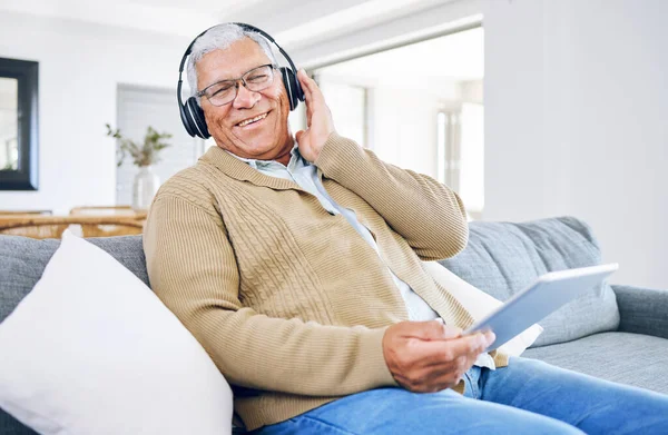 Portrait, home and old man with tablet, headphones and smile with connection, streaming music and radio. Senior person, technology and pensioner with headset, listening to audio and sound on a couch.