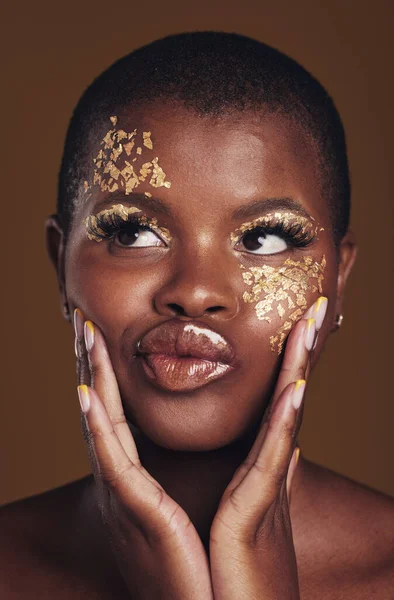 Art, fun and black woman in gold makeup on brown background, glitter paint or cosmetics. Shine, glow and silly face of African model in studio for beauty, fashion and aesthetic freedom in luxury skin.
