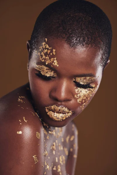 Art, facial on black woman with gold makeup and brown background, glitter paint and cosmetics. Shine, glow and African model in studio for beauty, fashion and aesthetic freedom in luxury skincare