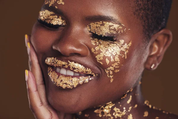 Black woman, face and gold makeup closeup with luxury dermatology and skincare mask with glitter. Sparkle, smile and beauty with rich and shine of cosmetics and model in a studio with facial art.