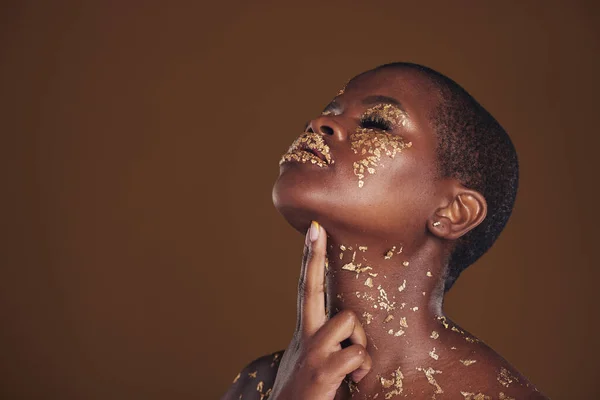 Profile, beauty and black woman with gold makeup, mockup and brown background with art, glitter paint and cosmetics. Shine, glow and African model in studio space for aesthetic, luxury and skincare