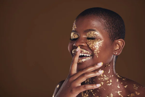 Happy laugh of black woman with gold makeup, mockup on brown background and glitter paint for cosmetics. Shine, glow and smile, African model in studio for facial beauty and funny aesthetic luxury