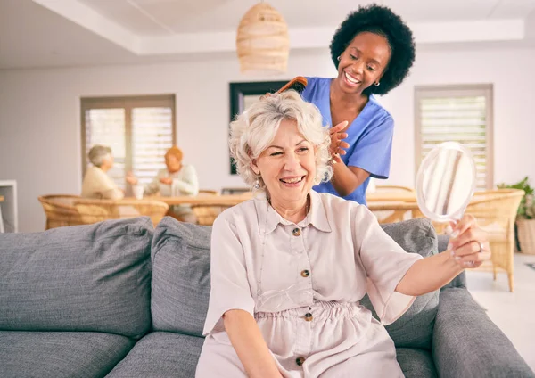 Nurse brush hair of happy mature woman in the living room of the modern retirement home for self care. Mirror, routine and African female nurse doing a hairstyle for an elderly patient in the lounge