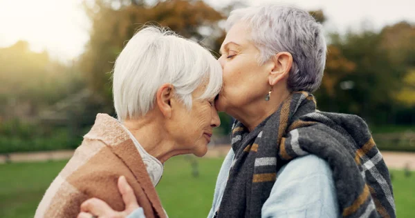 Senior woman kissing her friend on the forehead for affection, romance and bonding on outdoor date. Nature, commitment and elderly female couple in retirement with intimate moment in garden or park