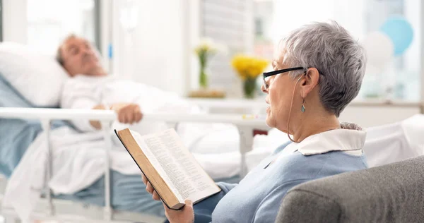 Healthcare, an old woman reading the bible to her husband during a visit and a couple in the hospital. Medical, retirement or religion with a senior wife and man patient at a clinic for faith in god.