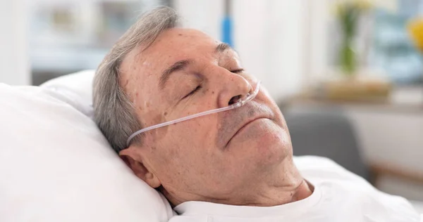 Oxygen, hospital bed and senior man sleeping with ventilation and breathing tube support in a clinic. Elderly patient, medical care and emergency room with male person at a doctor for healthcare.
