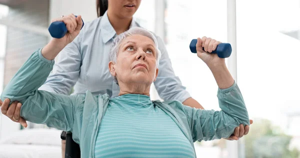 Woman with disability, physiotherapy and dumbbell exercise of healthcare rehabilitation, consulting or physical therapy assessment. Clinic, physiotherapist and support of senior patient in wheelchair.
