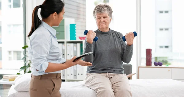 Physical therapy, senior patient with dumbbells and chiropractor with tablet, monitor progress and exercise. Help, support and women at clinic, weightlifting and elderly care with health and physio.