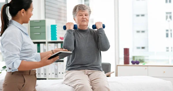Physical therapy, senior patient with dumbbells and chiropractor with tablet, monitor progress and exercise. Help, support and women at clinic, weightlifting and elderly care with health and physio.