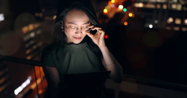 Glasses, tablet and Asian woman in night office, working late on project deadline or research. Tech, overtime and female employee with touchscreen reading email, report or proposal in dark workplace
