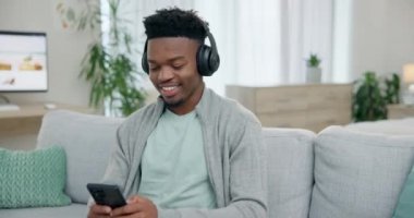 Mutlu siyahi adam, akıllı telefon ve kulaklıklar ses, radyo uygulaması ve ses aboneliği için koltukta. Cep telefonlu adam oturma odasında müzik dinliyor, podcast ve dijital multimedya arıyor..