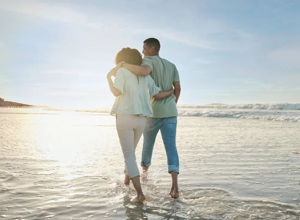 Love, hug and back of couple at the beach walking, bond and relax in nature on blue sky background. Ocean, love and rear view of man embrace woman at sea for travel, freedom and romantic walk in Bali.