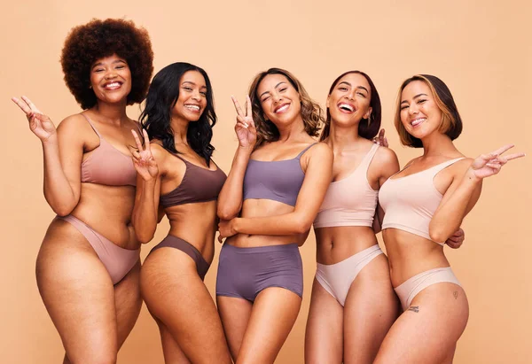 Body positive, peace sign and portrait of women in studio in underwear for wellness, beauty and self love campaign. Diversity, emoji and people on brown background for natural, skincare and inclusion.