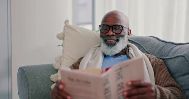 成熟的黑人 在家里客厅沙发上看书 快乐的 新奇的和非洲的人在休息室休息 学习文学和退休生活中的幻想故事 — 图库视频影像