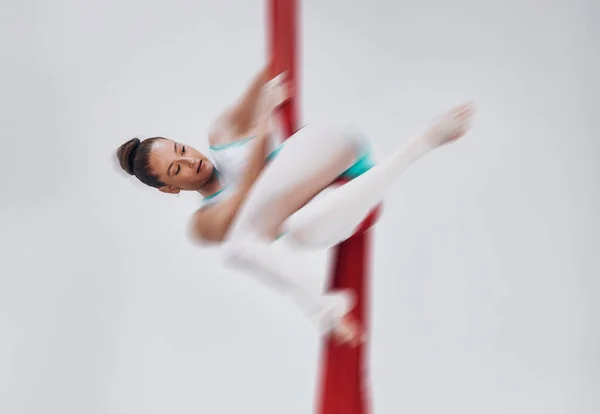 Gymnastics, woman and aerial silk with a acrobat in air for performance, sports and balance. Young athlete person or gymnast hanging on red fabric and white background with space, art and creativity.