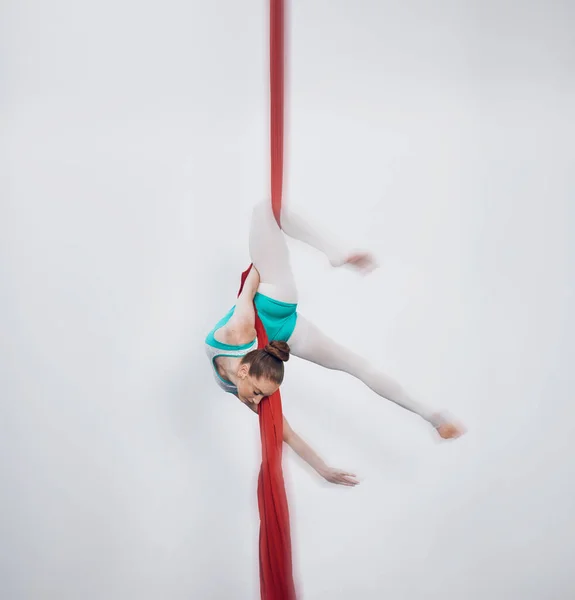 Gymnastics, acrobat and aerial silk with a sports woman in air for performance and balance. Young athlete person or gymnast hanging on red fabric and white background with space, art and creativity.