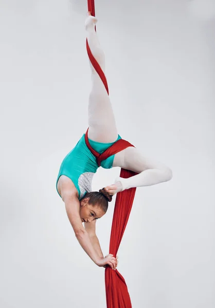 Gymnastics, aerial acrobat and silk with a woman in air for performance, sports and balance. Young athlete person or gymnast hanging on red fabric and white background with space, art and creativity.