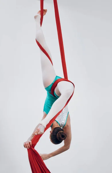 Performance, acrobat and aerial silk with a woman in air for gymnastics, sports and balance. Athlete person, dancer or gymnast hanging on red fabric and white background with space, art or creativity.
