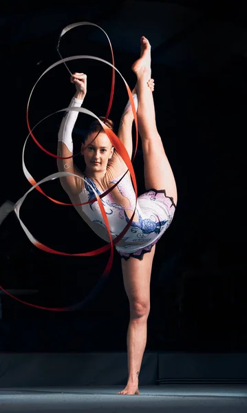 Woman, portrait and balance for ribbon gymnastics, sports performance or competition in dark concert arena. Flexible athlete, dancer and stretching for agile showcase, challenge and rhythm in contest.