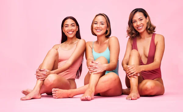 Beauty, bikini and group of women in studio, sitting together with smile and body positivity portrait. Diversity, summer fashion and happy swimwear models with self love, equality and pink background.