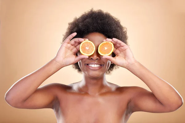 Orange fruits, skincare and woman on studio background for natural cosmetics, healthy benefits and nutrition. Happy african beauty model cover eyes with citrus for vitamin c, detox or eco dermatology.