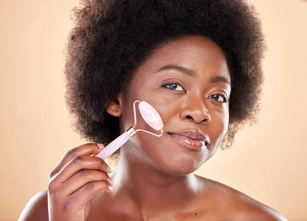 Black woman, face roller and portrait of beauty, rose quartz cosmetics and natural skincare on studio background. Happy model, facial massage and crystal tools for dermatology of lymphatic drainage.