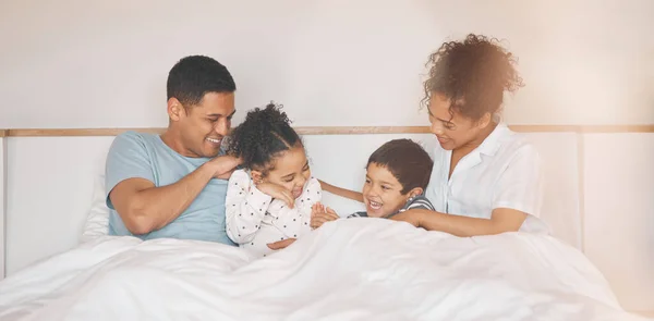 Happy, tickle and relax with family in bedroom for playful, morning and love. Care, support and wake up with parents and children laughing in bed at home for weekend, positive and resting together.