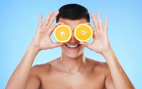 Happy, lemon and skincare with face of man in studio for health, detox and natural cosmetics. Vitamin c, nutrition and summer with person and fruit on blue background for self care, beauty and glow.