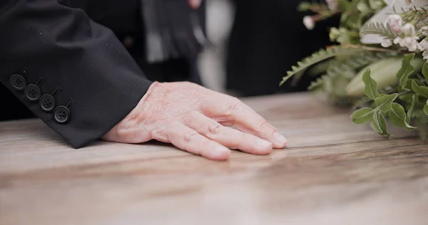 Death, funeral and hand on coffin in mourning, family at service in graveyard or church for respect. Flowers, loss and people at wood casket in cemetery with memory, grief and sadness at grave burial.
