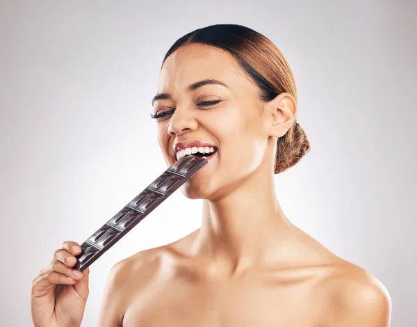 Skincare, diet and happy woman in studio with dark chocolate for anti aging benefits on white background. Sugar, beauty and lady model face, smile and eat candy bar for collagen, diet or pigmentation.