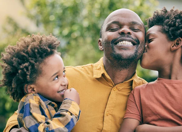 Kiss, love or father with happy kids in nature, park or field on fun holiday vacation together outdoors. Smile, black family or children siblings bonding to relax in garden for care, support or trust.