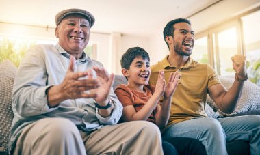 Baba, büyükbaba ve çocuk televizyon seyrediyor ve evde kanepede canlı yayın, gol ve destek için kutlama yapıyorlar. Erkek çocuk, kıdemli adam ve ebeveyn erkek aile takımı olarak bir arada ve heyecanlı esports taraftarı olarak alkışlıyorlar..