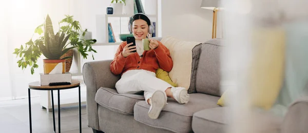 Asian woman, phone or music headphones on relax sofa in house or Japanese home living room. Smile,enjoy or happy student with mobile technology for podcast, dance radio or audio playlist app in comfo.