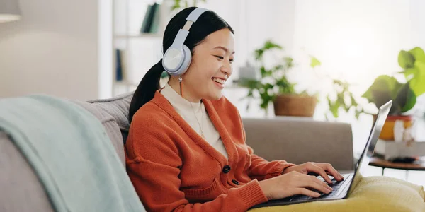 Laptop, headphones and asian woman on couch with work from home opportunity in online or website copywriting. Remote worker or person in china typing on her computer and listening to music at home.