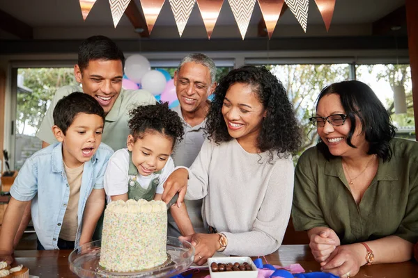 Family, birthday cake and excited at party to celebrate and cut slice together for dessert. Fun, happy and event for parents and grandparents with young children at a table for holiday celebration.