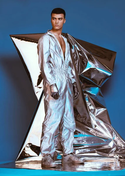 Holographic, vaporwave fashion and man with futuristic ski style with sci fi clothing in studio. Art, creative and male model with trendy, cool and cyberpunk designer clothes with blue background.