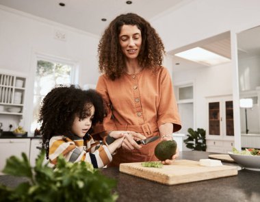 Yemek, avokado ve kızıyla birlikte yemek pişiren bir anne. Beslenmek için evlerinin mutfağında. Çocuğuna yeşil sebze yemeyi öğreten bir kadınla aile, sağlık ya da diyet.