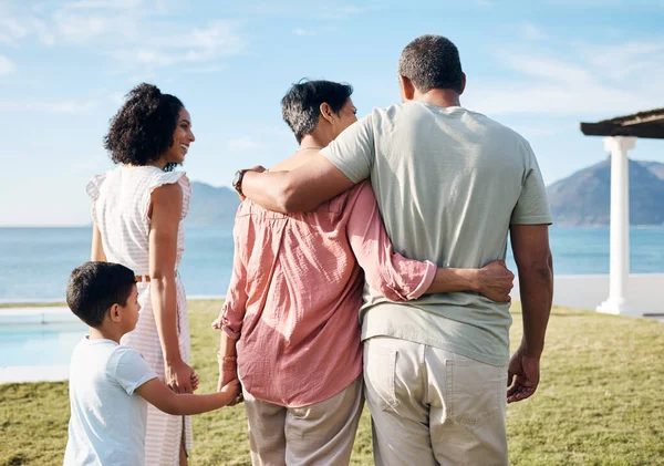 Back, summer and vacation by the sea with family outdoor together looking at a view of nature. Grandparents, mother and happy son by the ocean for love, holiday freedom or weekend getaway and travel.