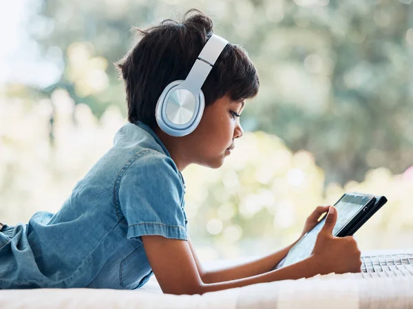 Boy child, tablet and headphones on bed, reading or idea with e learninng, movie and web video to relax. Male child, digital touchscreen and thinking in bedroom for games, music and streaming in home.