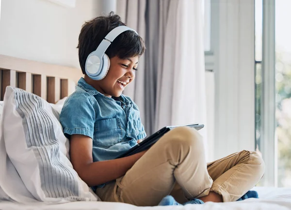 快乐的孩子和带着平板电脑的耳机躺在床上看搞笑电影 玩电子游戏或应用程序 男孩在家里用数字技术笑多媒体 听音乐或播放卡通片 — 图库照片
