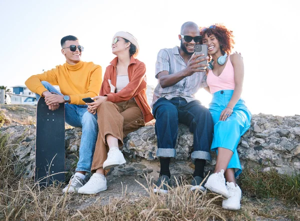 Gen z, friends and relax outdoor with phone, vacation and skateboard for selfie, memory and conversation in nature. Young men, women and students with smile, smartphone and summer memory in Cape Town.