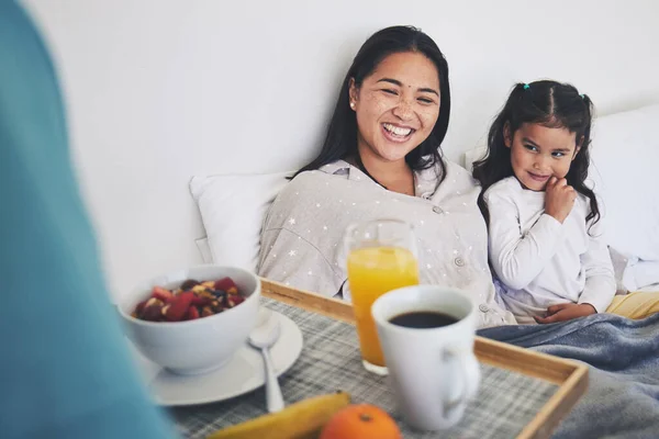 Mother and daughter with breakfast in bed while relaxing for mothers day surprise at home. Happy, smile and young mom resting with girl child with a healthy meal for brunch on weekend at their house