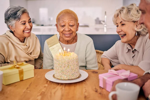 Senior women, birthday cake candle and party at a home with a present and gift with excited friends. Surprise, event dessert and retirement of elderly group at dining room table together with a smile.